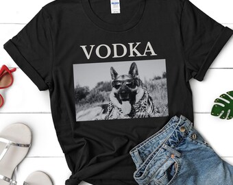 Może przedstawiać: Czarny T-shirt z nadrukiem "VODKA" w kolorze białym na przodzie. Pod tekstem znajduje się czarno-białe zdjęcie owczarka niemieckiego w okularach przeciwsłonecznych.