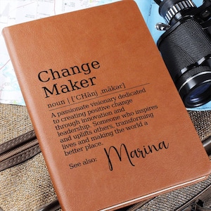 May include: A brown leather journal with the words "Change Maker" defined as "A passionate visionary dedicated to creating positive change through innovation and leadership. Someone who inspires and uplifts others, transforming lives and making the world a better place." The name "Marina" is written below the definition.