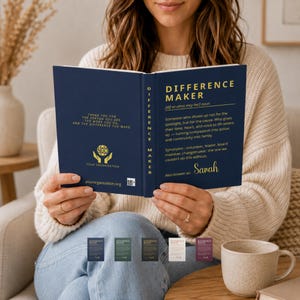 Op de afbeelding: Een marineblauw boek getiteld "DIFFERENCE MAKER" wordt opengehouden en toont tekst die de term en zijn synoniemen definieert. De omslag luidt "THANK YOU FOR THE PERSON YOU ARE AND THE DIFFERENCE YOU MAKE." Extra kleine boeken in verschillende kleuren staan onderaan.