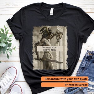 Könnte beinhalten: Schwarzes T-Shirt mit einer sepiafarbenen Grafik einer Frau mit einem Schwert und dem Text "Women Must Serve Men". Das Shirt hat auch den Text "Personalisiere mit deinem eigenen Zitat" und "Gedruckt in Europa".