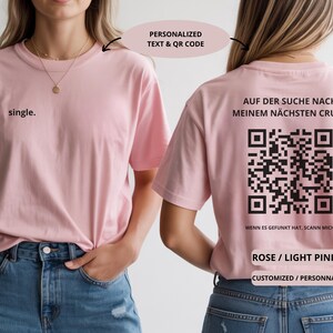 May include: Light pink t-shirt with the word "single" on the front. The back of the shirt features a QR code and the German text "AUF DER SUCHE NACH MEINEM N&Auml;CHSTEN CRUSH" and "WENN ES GEFUNKT HAT, SCANN MICH".