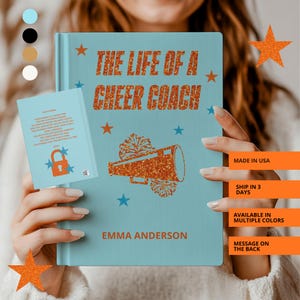 May include: A light blue book with the title "THE LIFE OF A CHEER COACH" in orange glitter text, with star accents and a megaphone graphic. The author's name, Emma Anderson, is also displayed. A smaller matching book is visible.