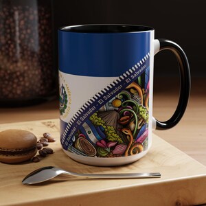 Puede incluir: Una taza de cerámica blanca con un borde y un asa negros. La taza presenta una ilustración colorida de la bandera de El Salvador con el texto "El Salvador - El Salvador - El Salvador" repetido alrededor del borde.