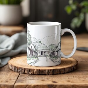 Puede incluir: Taza de cerámica blanca con una ilustración en blanco y negro de un pueblo con casas y una persona caminando por un sendero. La taza tiene un asa negra.