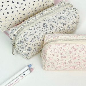 May include: Three rectangular zippered pouches made of cream-colored fabric with a ribbed texture. Two pouches feature a small dark blue floral pattern, while the smaller front pouch displays a delicate pink floral print. Each has a silver zipper.