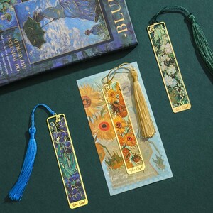 May include: Three gold metal bookmarks with colorful images and tassels. The bookmarks feature artwork by Van Gogh, including sunflowers, irises, and a starry night scene. The tassels are blue, gold, and green.