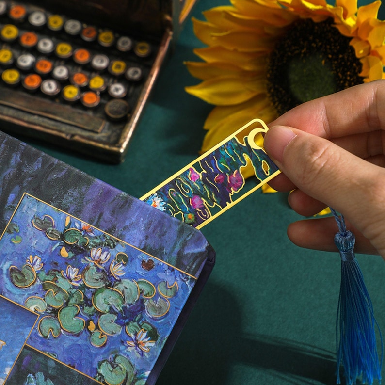 May include: A gold bookmark with a blue and purple floral design. The bookmark has a tassel on the end.