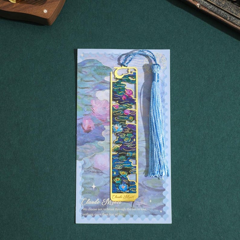 May include: A gold metal bookmark with a blue tassel. The bookmark features a colorful image of water lilies and the text "Claude Monet". The text below the image reads "We choose not to talk back through the tears in love, nothing more than tears of love."