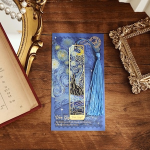 May include: A gold metal bookmark with a blue tassel. The bookmark features a reproduction of Vincent van Gogh's "Starry Night" painting. The bookmark is on a blue background with the text "Van Gogh Van Gogh" and "We choose not to break through the 25th in love, nothing more than fear of loss."