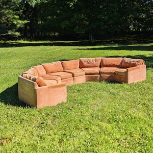 May include: A curved sectional sofa upholstered in a solid burnt orange fabric. The modular furniture piece features a low-profile design with multiple connected seat cushions and backrests, creating a continuous semi-circular seating arrangement.