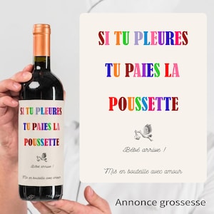 Peut inclure: Une bouteille de vin rouge avec un bouchon doré et une étiquette colorée. L'étiquette indique "SI TU PLEURES TU PAIES LA POUSSETTE" et "Bébé arrive!". Une carte à côté de la bouteille a le même texte.