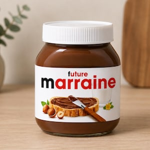 Peut inclure: Un pot en verre rempli de pâte à tartiner aux noisettes de couleur brune avec un couvercle blanc. L'étiquette porte le texte future marraine en lettres noires et rouges. Une illustration montre une tranche de pain tartinée, un couteau et des noisettes.
