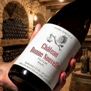 Peut inclure: Une bouteille de vin en verre foncé avec une étiquette blanche illustrée d'une cigogne portant un bébé. Le texte indique Cuvée Spéciale, Château Bonne Nouvelle, Futur Papi, Grand Cru 2027, et Mis en bouteille avec amour.