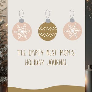 Puede incluir: Un diario de vacaciones con fondo crema y detalles dorados y rosas. La portada presenta tres ilustraciones de adornos navideños con diseños de copos de nieve y líneas onduladas. El texto dice "THE EMPTY NEST MOM'S HOLIDAY JOURNAL."