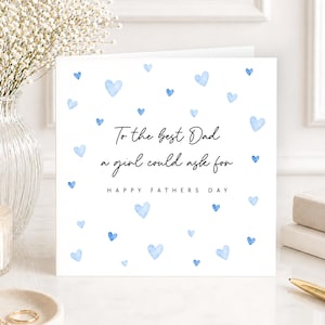 K&ouml;nnte beinhalten: Eine quadratische wei&szlig;e Gru&szlig;karte mit verstreuten hellblauen Aquarellherzen. Der Text lautet: To the best Dad a girl could ask for, gefolgt von HAPPY FATHERS DAY in schwarzer Schrift. Die Karte liegt auf einer wei&szlig;en Oberfl&auml;che.