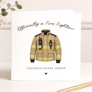 May include: A square greeting card with a white background featuring a tan firefighter jacket with yellow reflective stripes, a black radio, and a badge. The text reads "Officially a Fire Fighter!" at the top and "CONGRATULATIONS JORDAN" at the bottom.