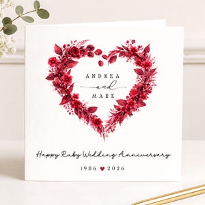 May include: A square white greeting card featuring a heart-shaped wreath of deep red flowers and leaves. The centre text reads ANDREA and MARK. Below the heart, the text reads Happy Ruby Wedding Anniversary followed by 1986, a red heart, and 2026.