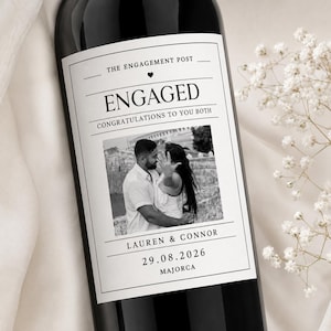 May include: A dark wine bottle with a white rectangular label featuring the text THE ENGAGEMENT POST, ENGAGED, CONGRATULATIONS TO YOU BOTH, LAUREN & CONNOR, 29.08.2026, and MAJORCA, along with a black and white photograph of a couple embracing.