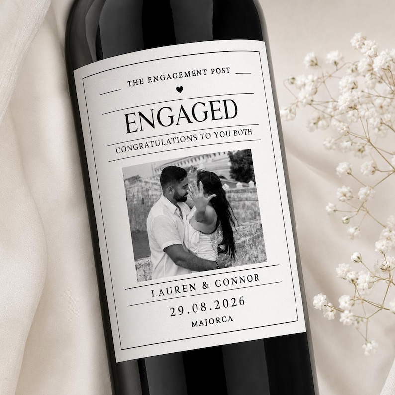May include: A dark wine bottle with a white rectangular label featuring the text THE ENGAGEMENT POST, ENGAGED, CONGRATULATIONS TO YOU BOTH, LAUREN & CONNOR, 29.08.2026, and MAJORCA, along with a black and white photograph of a couple embracing.