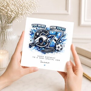 May include: A square birthday card featuring the text YOU WERE NOW YOU'RE 67 in blue and black. The design includes a large number 67, a game controller, a soccer ball, and a skateboard. Below, it reads HAPPY BIRTHDAY TO A VERY SPECIAL SON and Lucas.