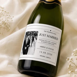 May include: A dark green glass bottle with a white rectangular label featuring a black and white photograph of a couple. The text reads: THE WEDDING POST, JUST MARRIED, WISHING YOU LOVE, LAUGHTER & HAPPILY EVER AFTER, ABBIE & DAVID, 14.08.2026, RHODES, GREECE.