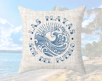 May include: Square decorative pillow with a textured beige background. The pillow features a blue circular design with the words "LAS PLAYAS SON DEL PUEBLO" and a stylized sun and waves.