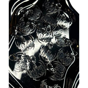 May include: A silver tray with multiple silver charms in the shape of a scorpion. The charms are arranged in a random pattern on the tray.