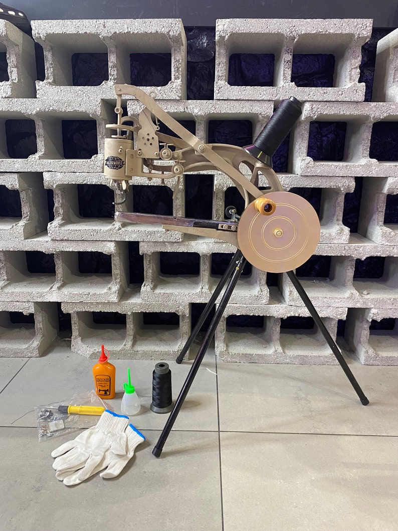 May include: A silver shoe sewing machine with a black thread spool and a gold-colored foot pedal. The machine is on a black tripod stand. There are two bottles of oil, a spool of thread, a pair of white gloves, and a tool in the image.