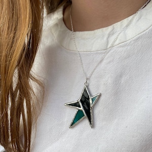 May include: A silver chain necklace with a stained glass star pendant. The star is made of black and teal glass.