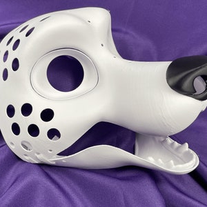 Op de afbeelding: Witte, onafgewerkte hondenkop voor een fursuit met een zwarte neus en open mond. De kop heeft een groot ooggat en een reeks kleine gaten aan de zijkant.
