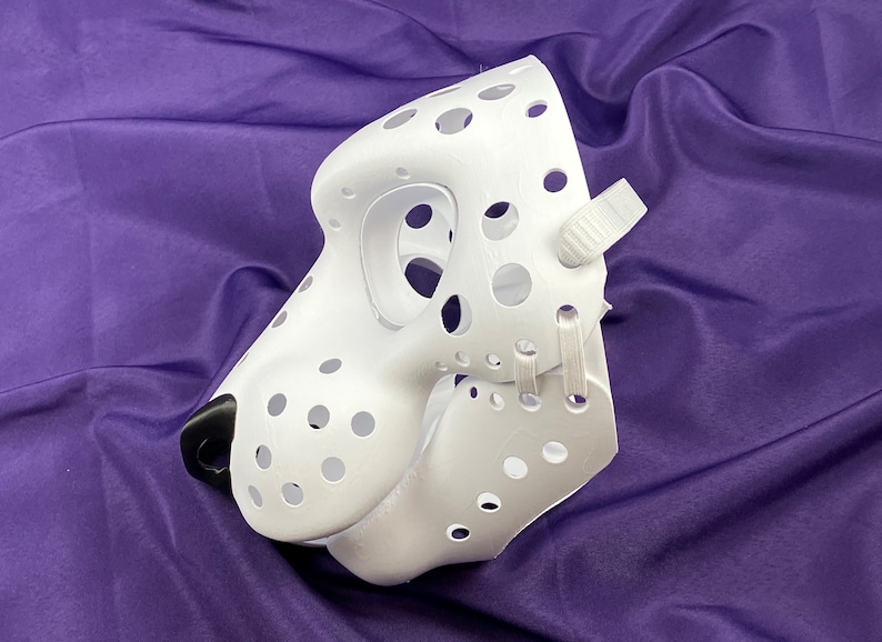 May include: White furry mask with a black nose and many small holes. The mask has white straps on the side.