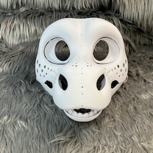 May include: White unpainted furry animal mask with holes for eyes and a mouth. The mask has a textured surface and is made of a hard material.