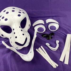 May include: White plastic mask with holes, separate white plastic pieces for eyes, nose, and teeth, and white elastic straps. The mask is for a furry costume.