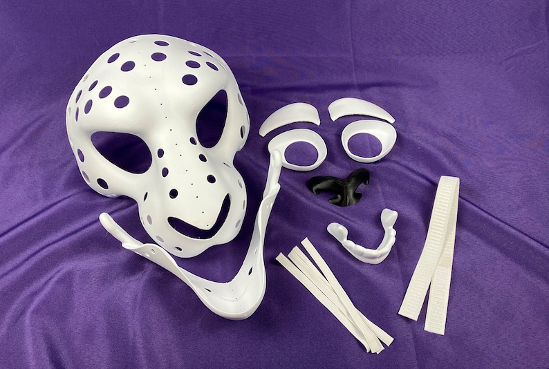 May include: White plastic mask with holes, separate white plastic pieces for eyes, nose, and teeth, and white elastic straps. The mask is for a furry costume.
