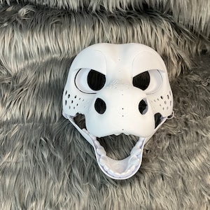 May include: White unpainted furry animal mask with open mouth and visible teeth. The mask has large black eyes and a textured nose.