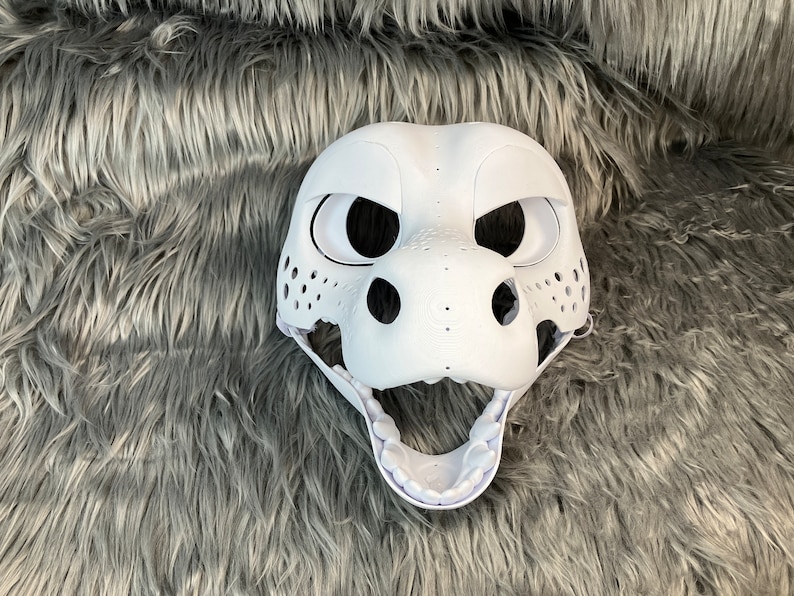 May include: White unpainted furry animal mask with open mouth and visible teeth. The mask has large black eyes and a textured nose.