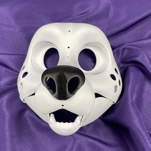 Op de afbeelding: Witte, ongeverfde vachtdiermasker met een zwarte neus en een open mond. Het masker heeft gaten voor de ogen en een stippenpatroon.