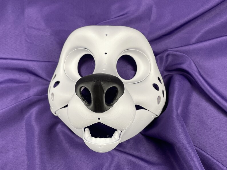 Op de afbeelding: Witte, ongeverfde vachtdiermasker met een zwarte neus en een open mond. Het masker heeft gaten voor de ogen en een stippenpatroon.