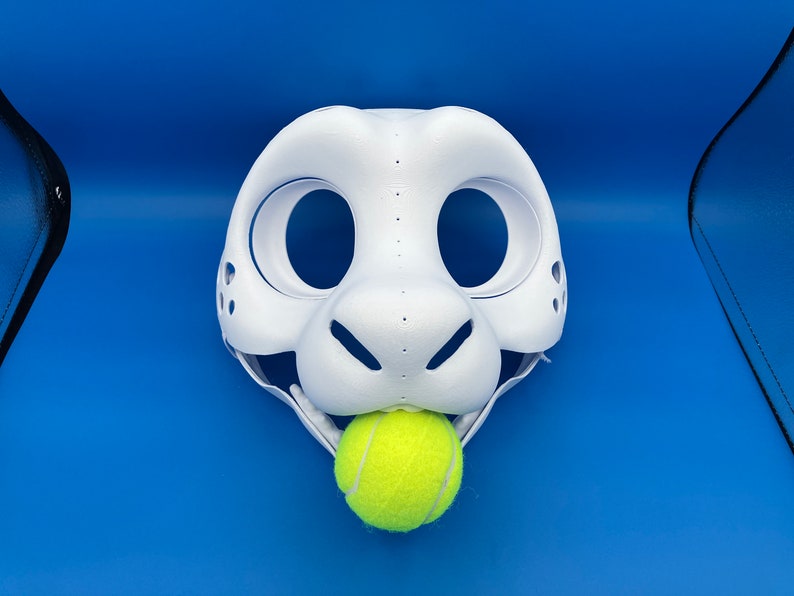 K&ouml;nnte beinhalten: Wei&szlig;e pelzige Tiermaske mit gro&szlig;en Augenl&ouml;chern und einer kleinen Nase. Die Maske ist offen und hat einen gelben Tennisball im Maul.