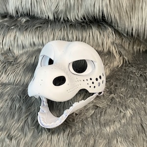 May include: White unpainted furry animal mask with holes for eyes, nose, and mouth. The mask is made of a hard plastic material and has a textured surface.