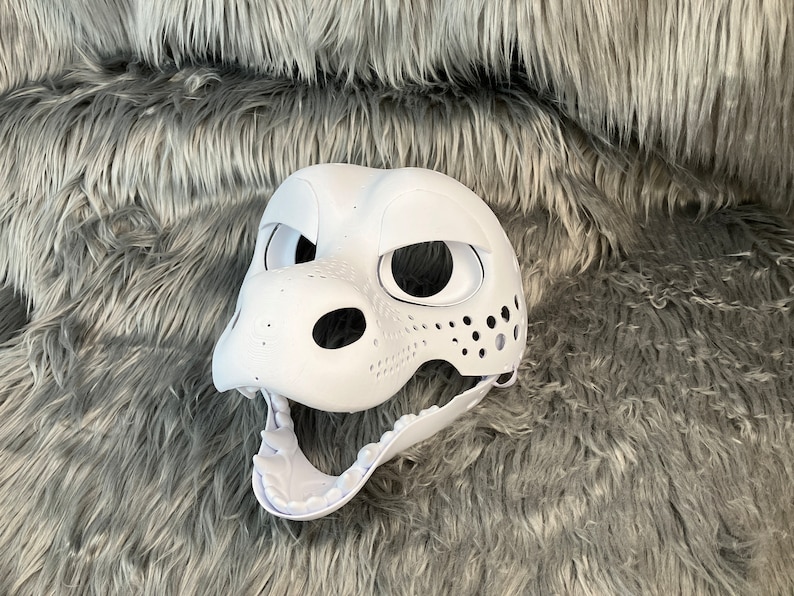 May include: White unpainted furry animal mask with holes for eyes, nose, and mouth. The mask is made of a hard plastic material and has a textured surface.