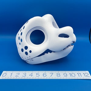 K&ouml;nnte beinhalten: Wei&szlig;e, unlackierte, 3D-gedruckte Tierkopfmaske mit einer strukturierten Oberfl&auml;che und einer Reihe von L&ouml;chern. Die Maske ist teilweise ge&ouml;ffnet und zeigt das Innere des Mundes. Ein Lineal im Vordergrund zeigt, dass die Maske etwa 18 cm lang ist.