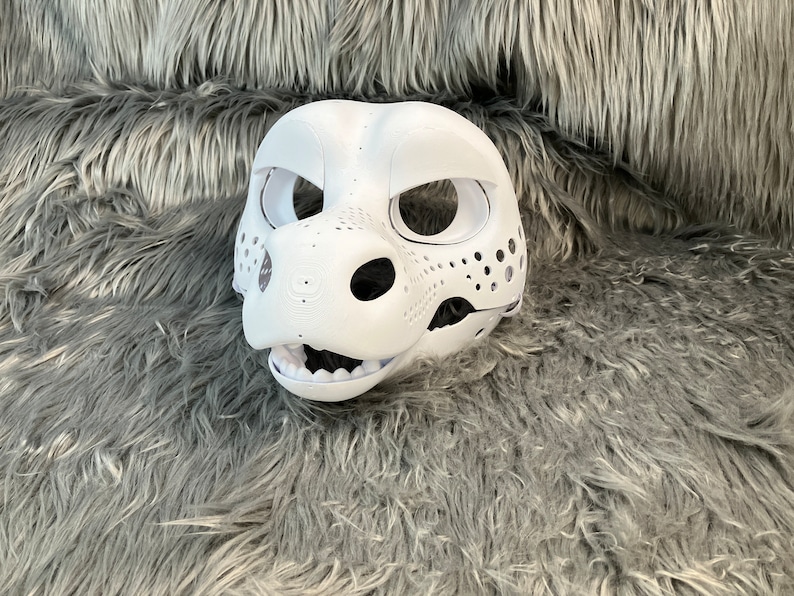 May include: White unpainted furry animal head mask with holes for eyes and nose. The mask is on a gray fluffy surface.