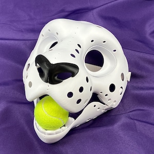 May include: White furry animal mask with black nose and open mouth holding a yellow tennis ball.