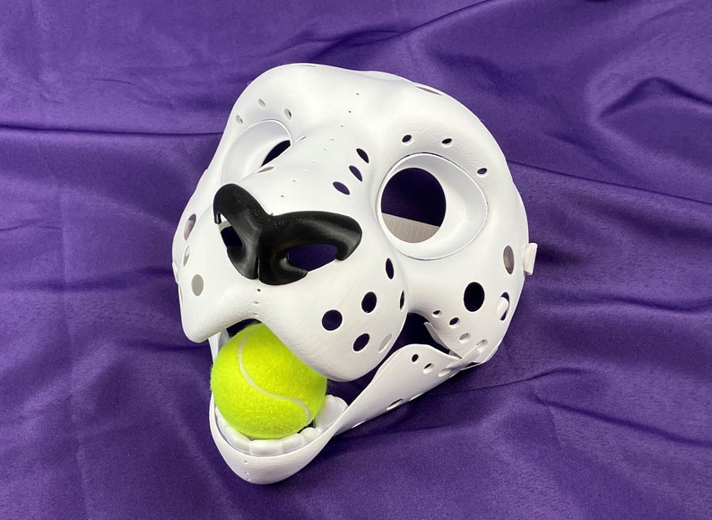 May include: White furry animal mask with black nose and open mouth holding a yellow tennis ball.