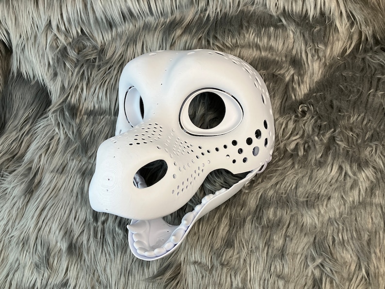 May include: White unpainted furry animal head base with holes for eyes and nose. The mouth is open and has teeth.