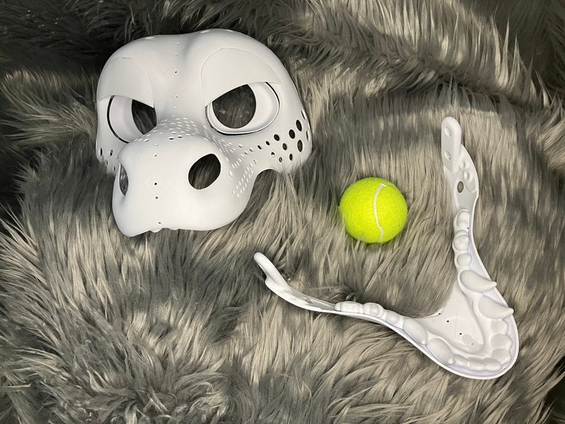 May include: White unfinished furry mask with a textured nose and eye holes. A white plastic jaw piece and a yellow tennis ball are also pictured.