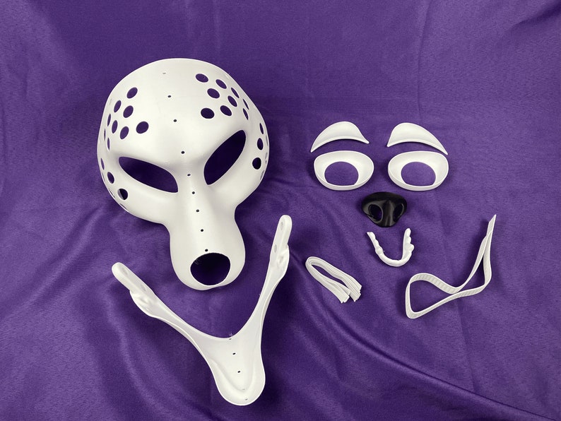 Op de afbeelding: Witte plastic masker met gaten en een aparte set witte plastic gezichtskenmerken, inclusief ogen, neus en mond.