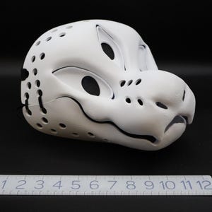 May include: White furry mask with black detailing and a textured surface. The mask has a snout, eyes, and a mouth. The mask is made of a lightweight material and has a comfortable fit.
