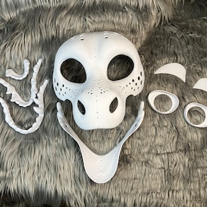 May include: White unfinished plastic mask with separate pieces for eyes, nose, and teeth. The mask is designed to look like a dragon or other fantasy creature.